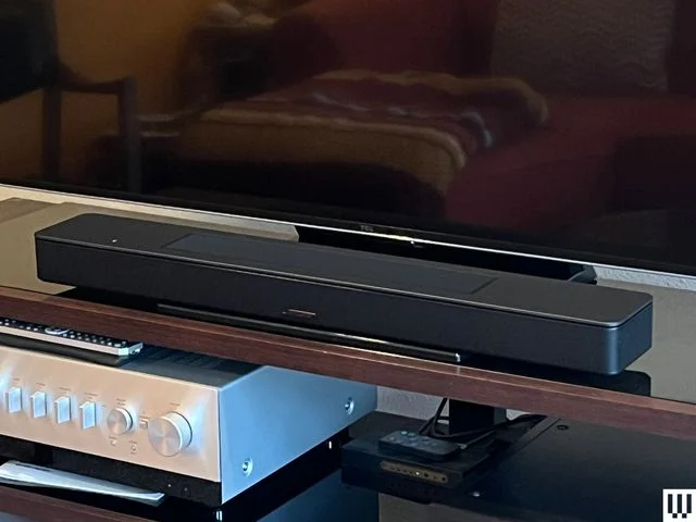 Bose Smart Soundbar, a long narrow black device, sitting at the base of a large flatscreen tv